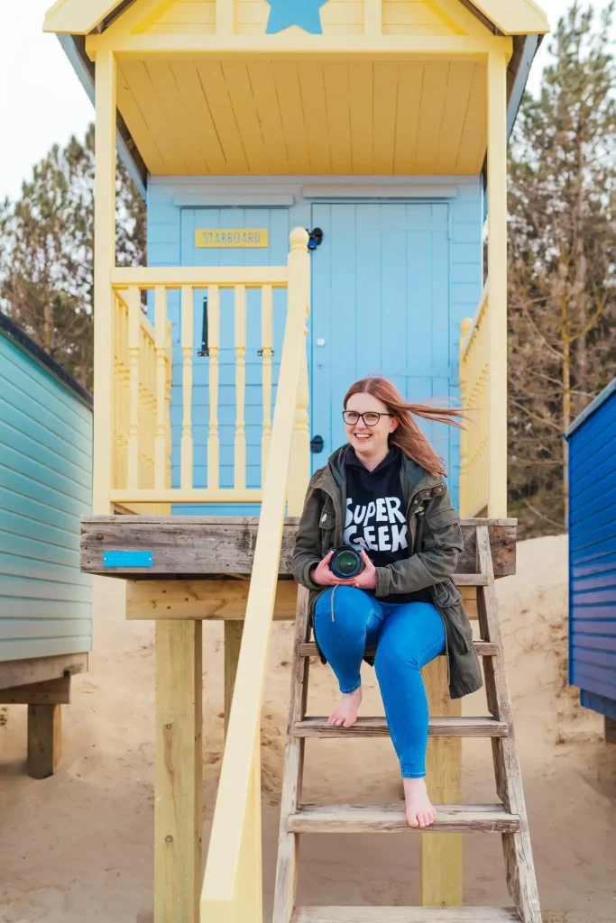 Kirsty Is sat on the steps of a blue and yellow beach hut.