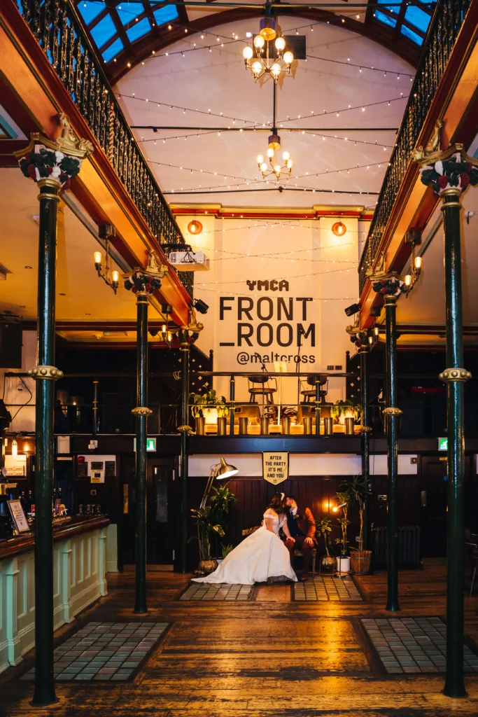 Couple sat kissing during a quiet moment under a sign that reads after the party its me and you. The rooms is dark and it feels intimate.