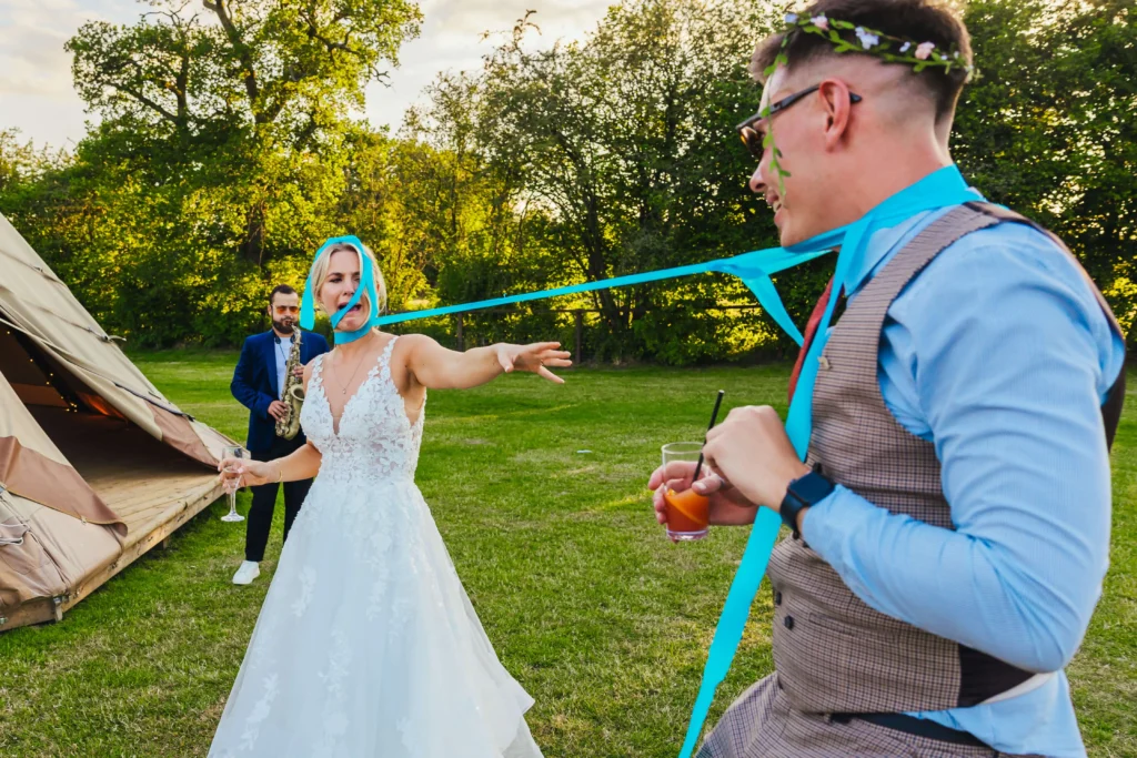 Bride and guest are tied together with a bunch of blue streamers. Bride is pulling a funny face whilst the guest smiles on.