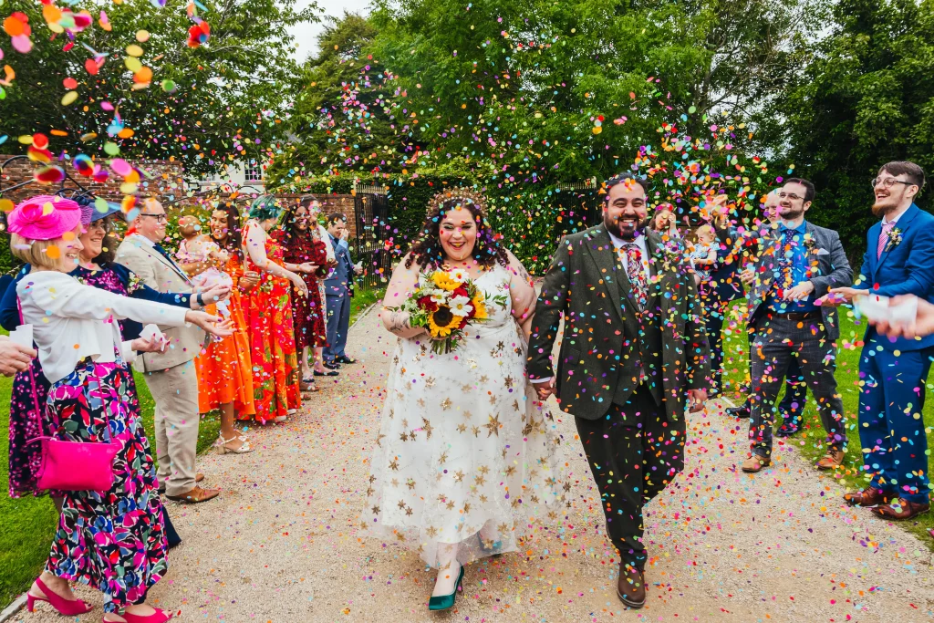 Couple walking through brightly confetti tunnel. Bride is wearing the most beautiful dress with stars on it