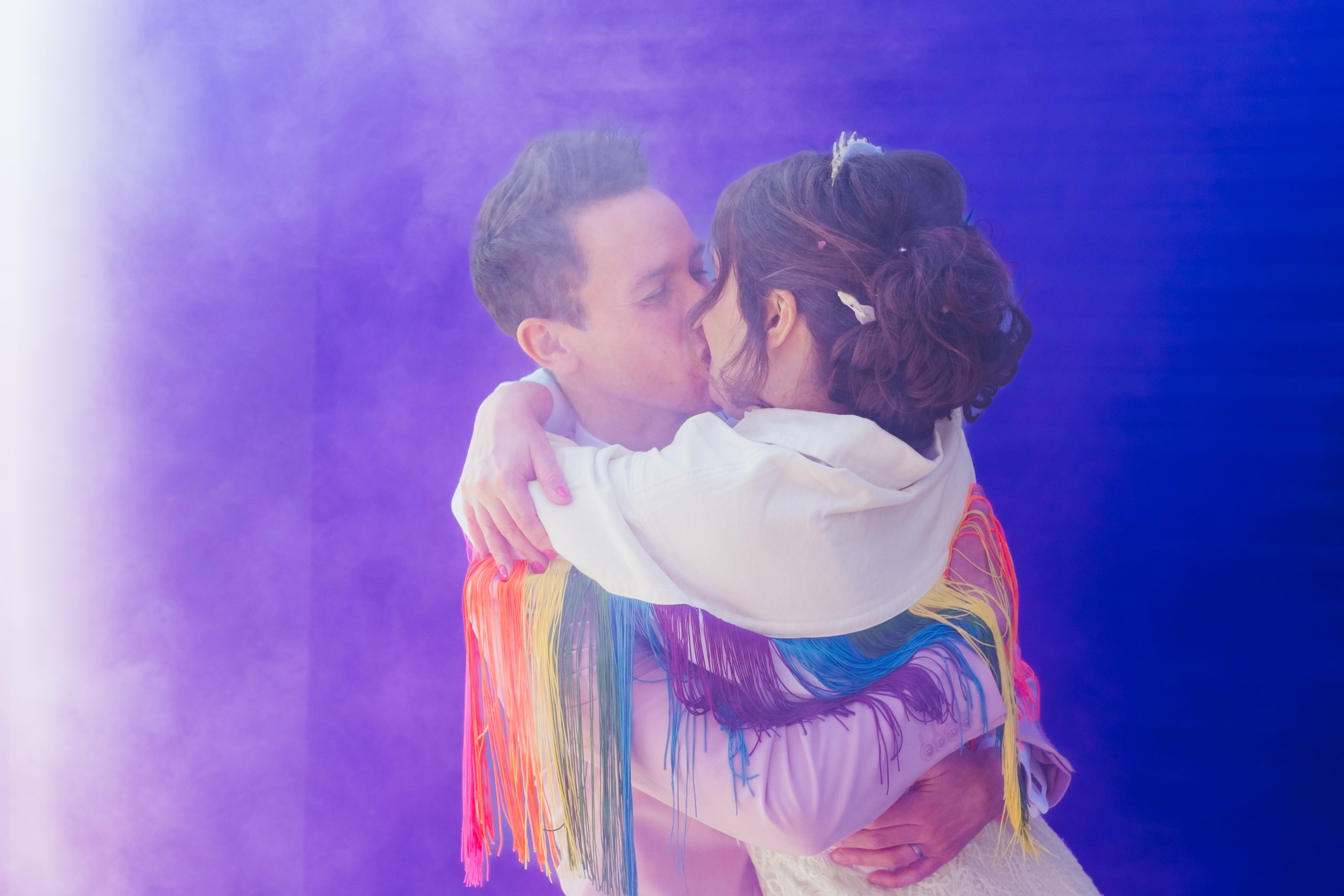 Couple surrounded by purple smoke. Bride is wearing a rainbow fringe jacket