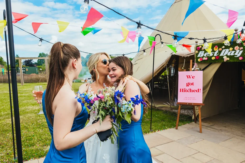 Bride kissing bridesmaid on her head tipi in the background and lots of bunting