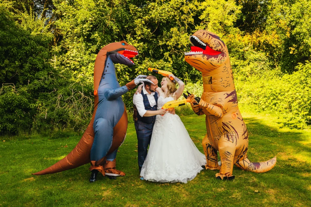 Couple holding nerf guns whilst being flanked by two people in blow up dinosaur suits.