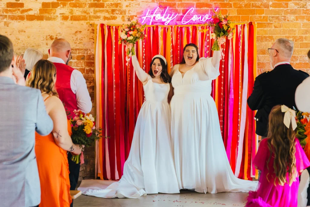 Couple holding their bouquets in the air after being announced married both have excited expressions on their faces