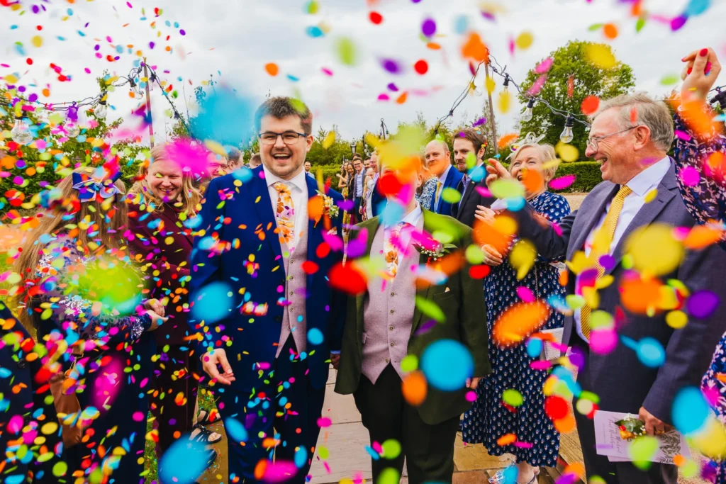 Couple walking through rainbow confetti and their smiling guests