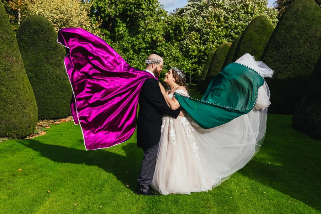 Couple photo in Holme Pierrepont Hall grounds, they're both wearing capes which are flying in the wind