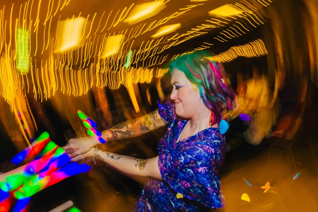 Guest dancing on dance floor surrounded by disco lights they're holding a foam glow stick and wearing a dinosaur dress
