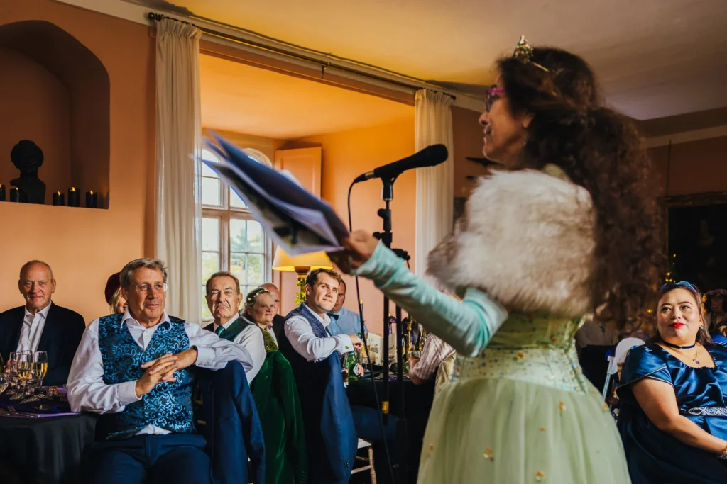 Mother of the bride giving a speech at her wedding with all the guests watching on all are smiling and listening intently.