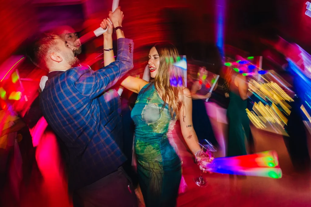 Guests dancing during DJ set at wedding their are light trails behind them and they're holding rainbow glow sticks