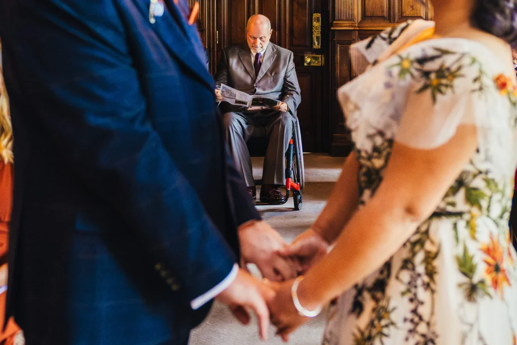 Close up of wedding guest reading wedding paper during a couples ceremony. The image is taken through the couples arms as they say their vows.