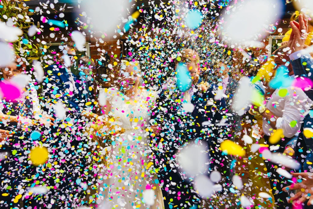 Couple walking into colourful explosion of confetti and bubbles after their wedding ceremony.