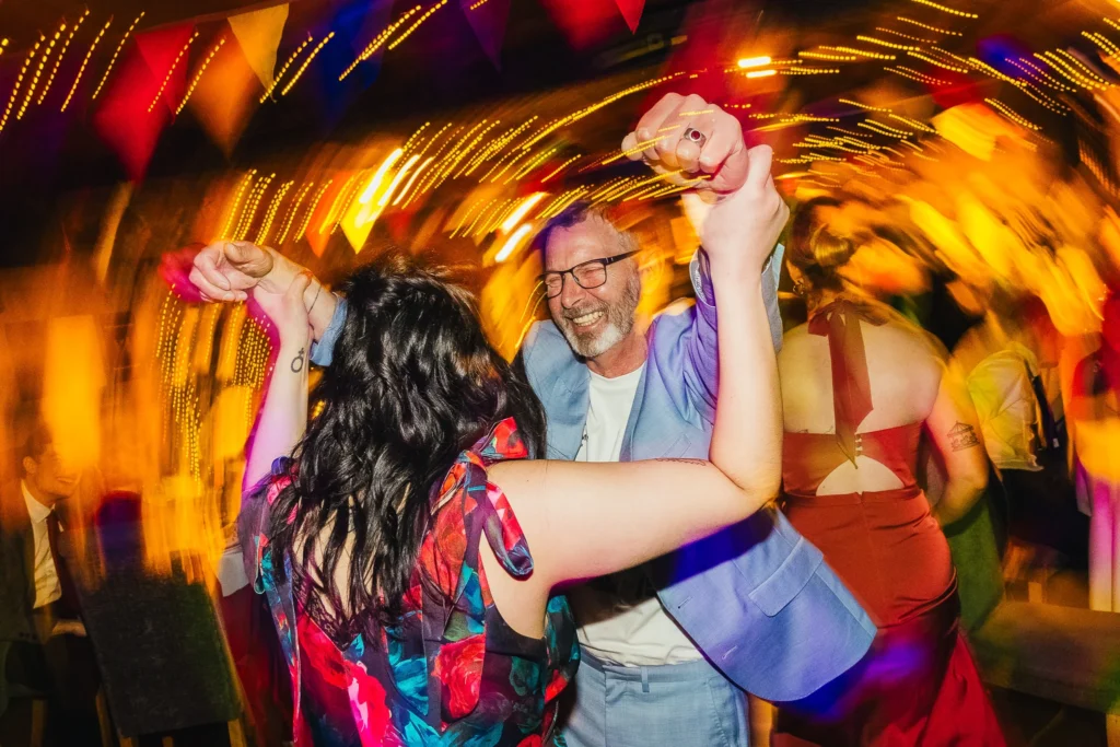 Two guests dancing in light trails on wedding dance floor. both are smiling and dancing like no ones watching