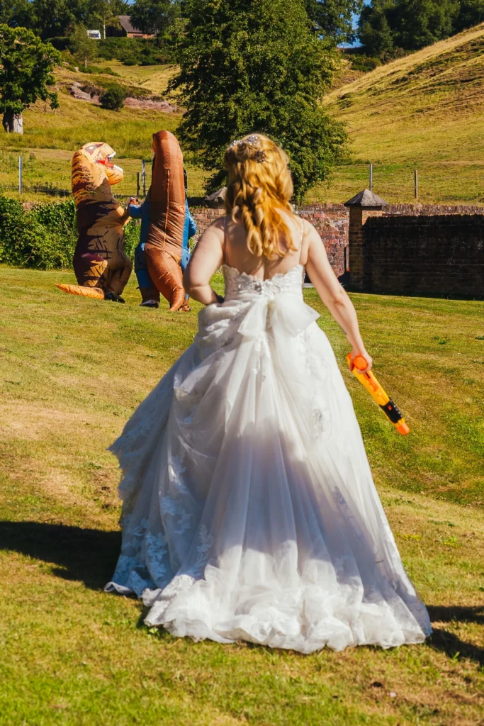Bride following two blow up dinosaurs with a nerf gun during her wedding reception