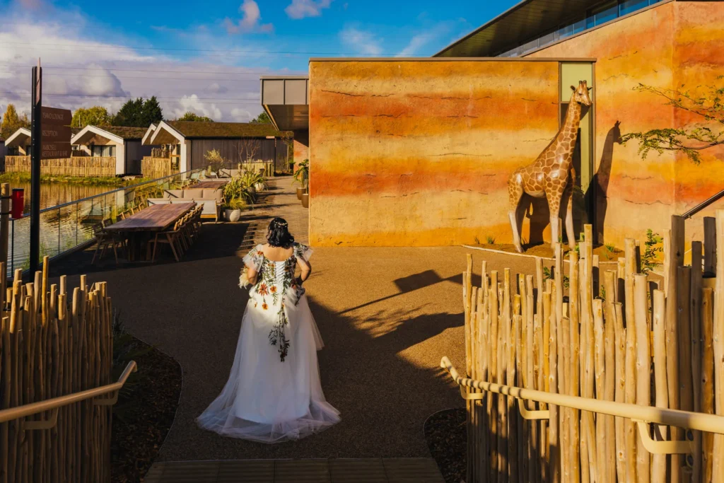 Bride walking through The Reserve at Chester Zoo in her wedding dress which is white with embroidered flowers