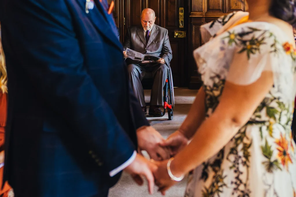 guest reading a wedding newspaper during the wedding ceremony the bride and groom are blurry in the foreground holding hands