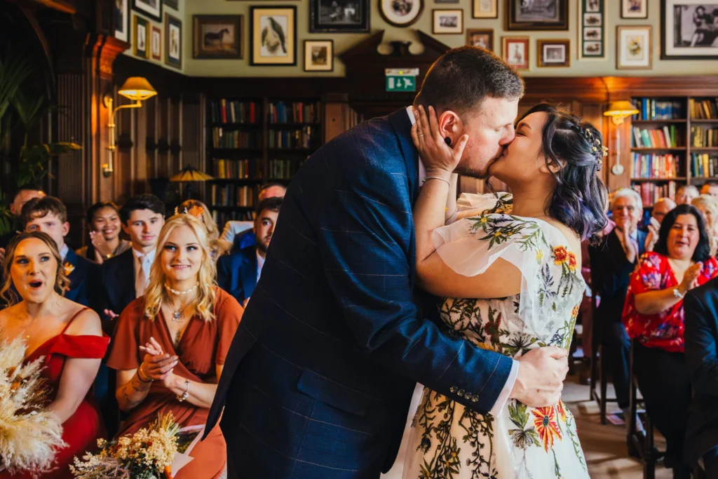bride and groom sharing their first kiss during their wedding ceremony whilst guest clap in the background.