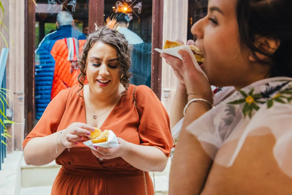 Bride eating cake in the foreground whilst her bridesmaid is just about to tuck into a cupcake behind