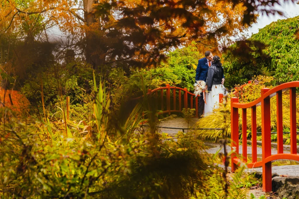 couple stood on a bridge in the Japanese garden at Chester Zoo they are framed by orange leaves