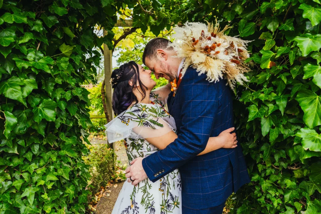 couple laughing together during portraits they are framed by green leaves. Bride is holding her bouquet on grooms shoulder