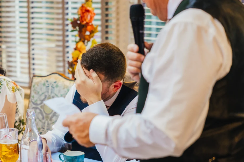 groom is face palming whilst listening and laughing at his dads speech