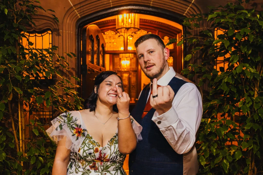 couple are flipping the wedding photographer off with their ring fingers. One is pulling a funny face whilst the other looks proud as punch