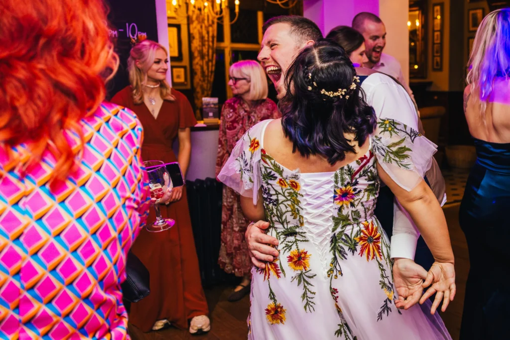 groom is laughing at one of the guests whilst he dances with is bride