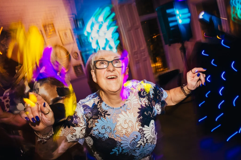 wedding guest is pulling a funny face at the camera whilst busting a move on the dance floor. there are light trails behind them