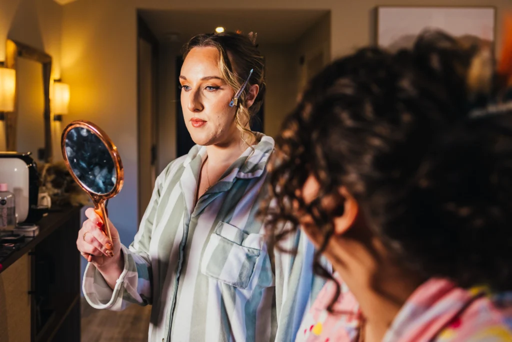 Bridesmaid checking her make up in a small mirror she's lit by a spotlight.