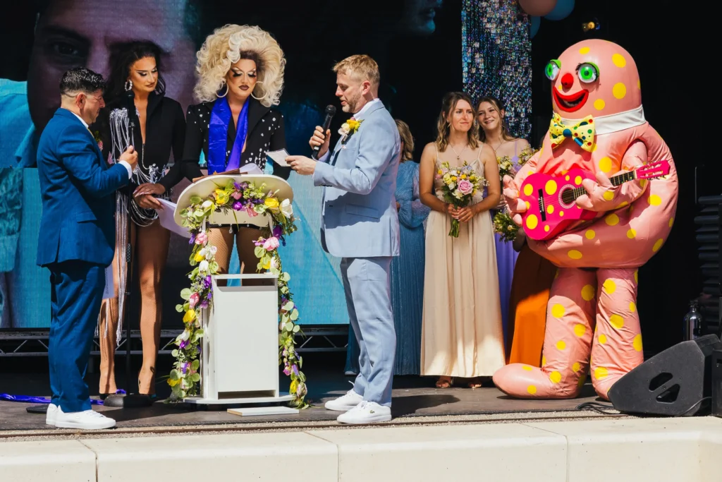 couple of stage during wedding ceremony, two gorgeous drag queens are conducting the ceremony and mr blobby is playing a pink spotty guitar