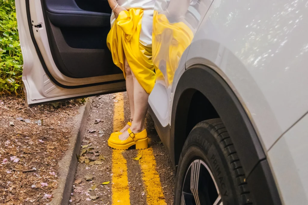 Bride exiting car she's wearing yellow shoes and a yellow dip dyed dress you can see the reflection in the car door.