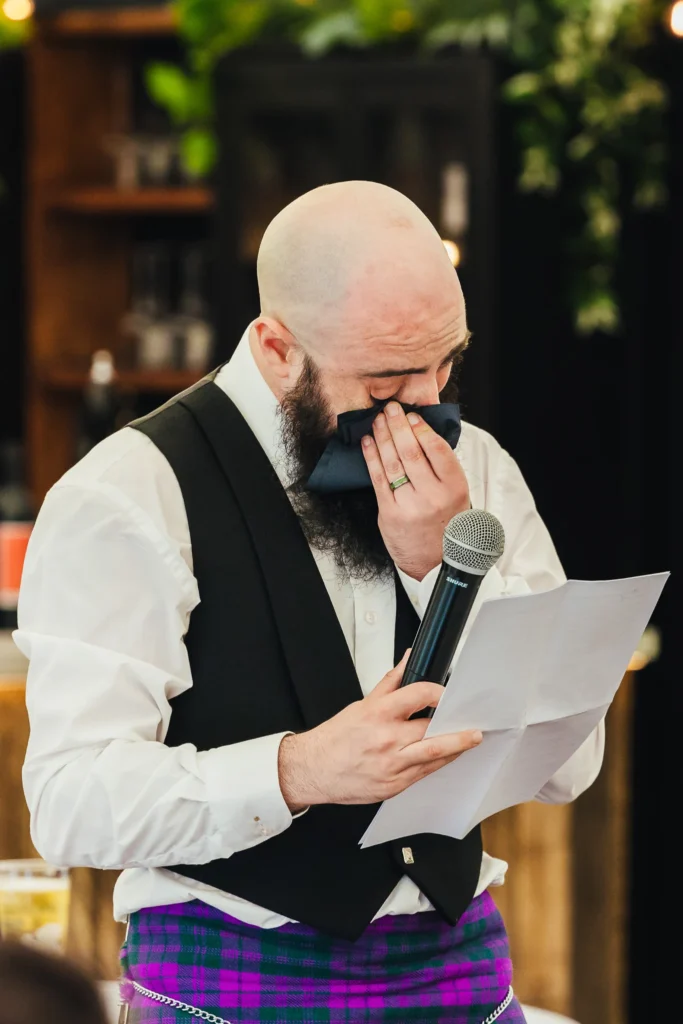 Groom getting emotional during speeches at his wedding. He's wiping away tears as he reads from his pages.
