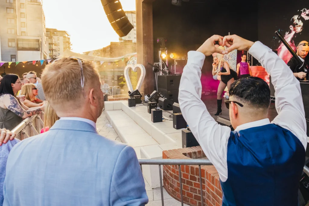Couple watch on as lady gaga tribute rocks the stage. One of the couple has his hads in a heart shape over his head which frames gaga perfectly.