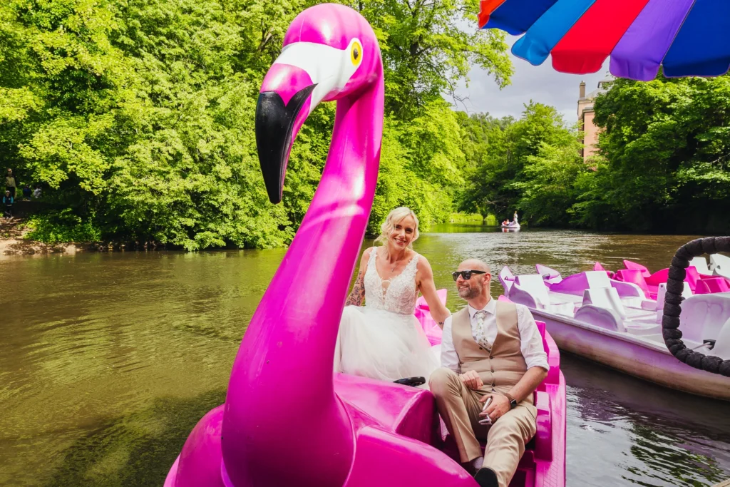 Couple on a giant Pink flamingo boat on the river at Matlock Bath. Groom is wearing shades and the bride looks stunning in her glittery dress.