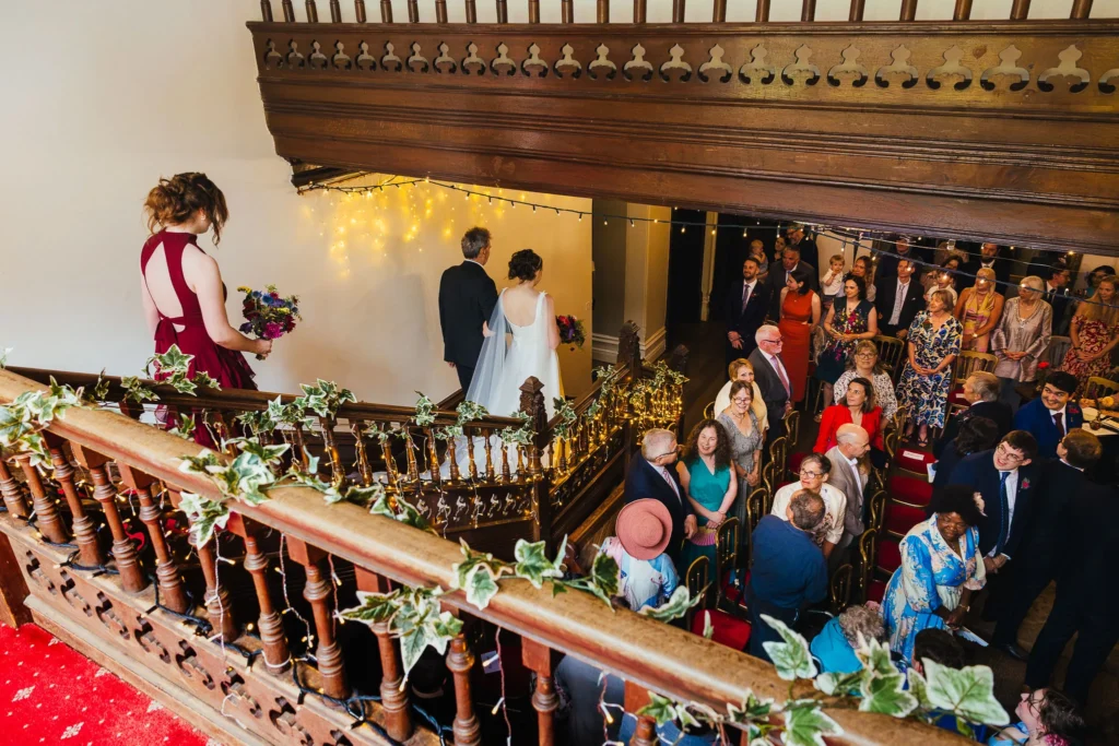 Bride and her dad make their way down the stairs at Hargate hall whilst the groom and the guests looks up at her from below.