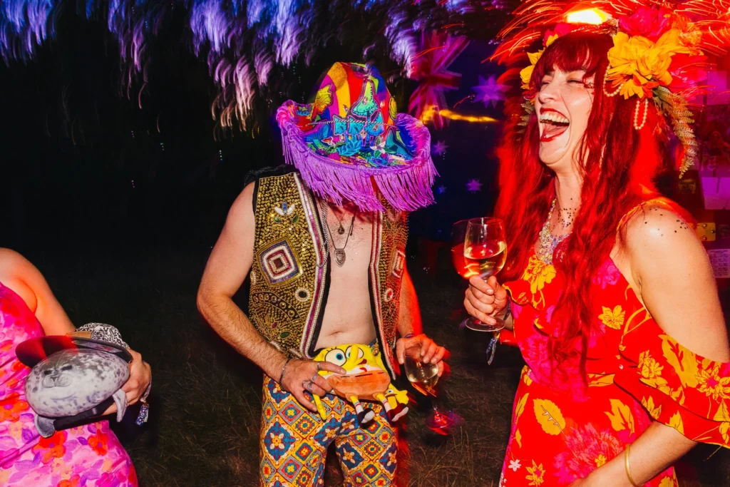 Guests partying the night away in festival attire one wears a colourful cowboy hat and a Spongebob bumbag