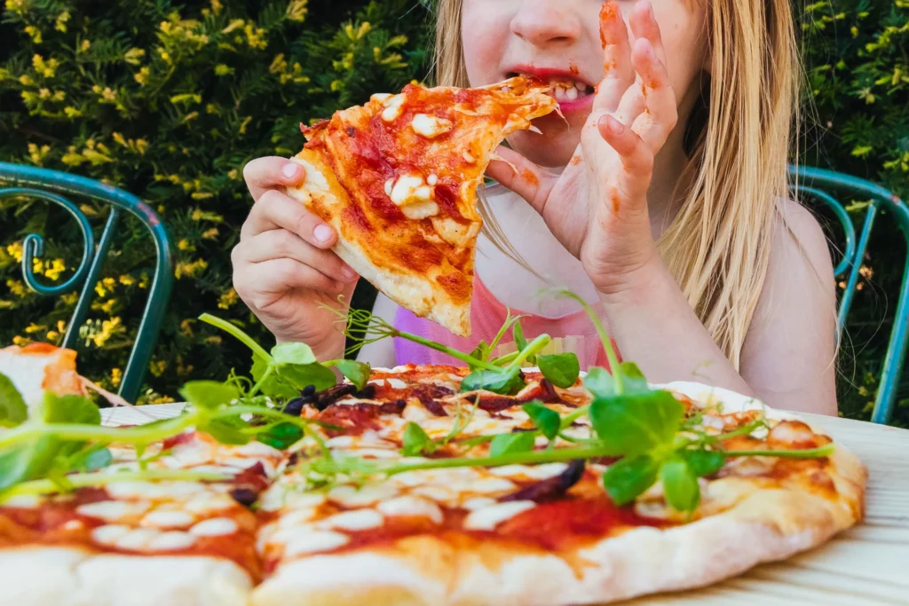 Close up of child eating a yummy pizza during a wedding breakfast, they're covered in pizza sauce.