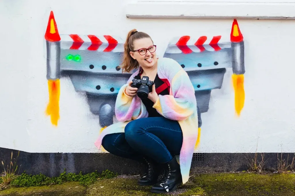 Kirsty crouching with her camera in front of a rocket mural