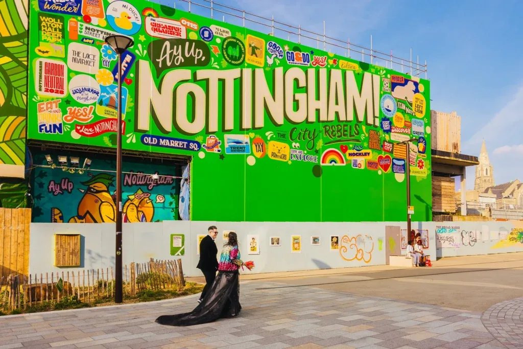 Couple walking past the giant green Ay Up Nottingham sign on their wedding day