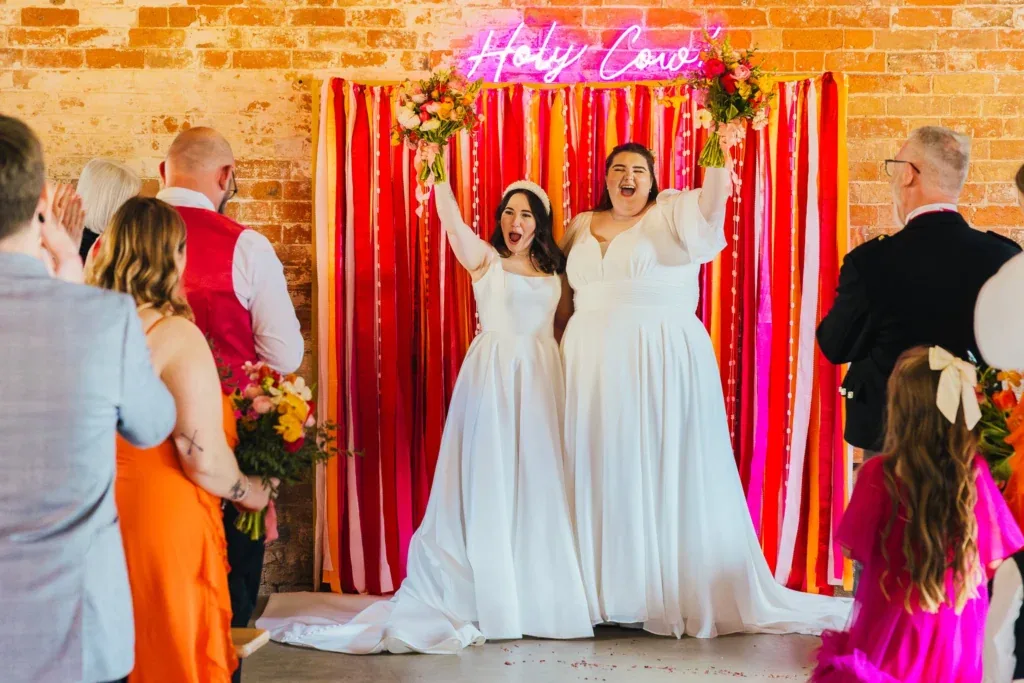 Two brides in front of a neon sign at The Old Cow Shed